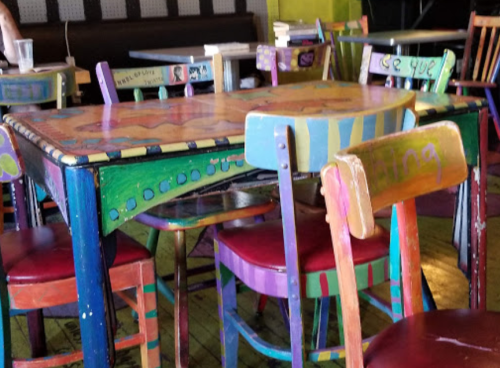 Colorful, hand-painted tables and chairs in a vibrant café setting.