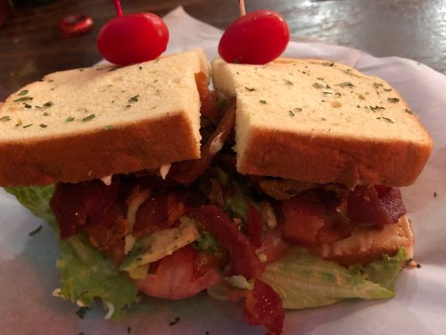 A hearty sandwich with layers of bacon, lettuce, and sauce, topped with two cherry tomatoes on toothpicks.
