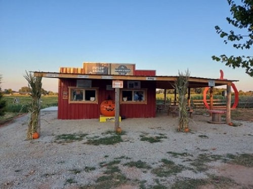 A rustic red building with pumpkins outside, surrounded by fields and a clear blue sky.