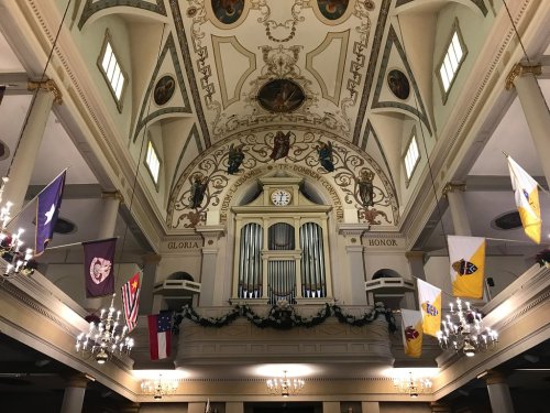 Interior of a church featuring ornate ceiling artwork, an organ, and various flags hanging from the walls.