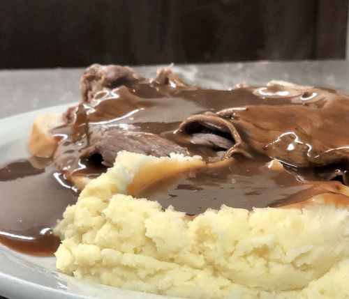 A plate of mashed potatoes topped with gravy, accompanied by slices of beef covered in brown sauce.