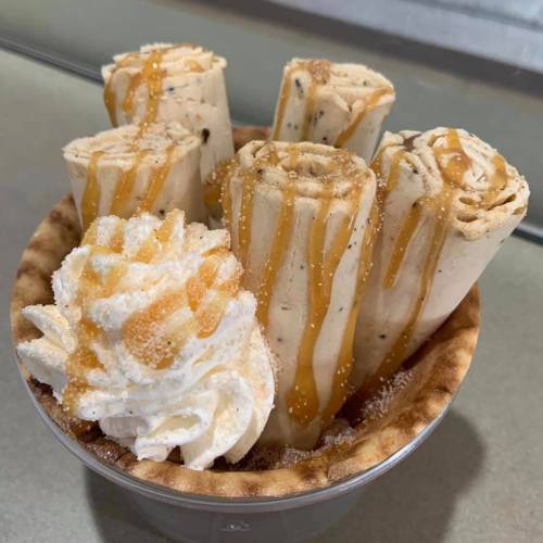 A bowl of rolled ice cream topped with whipped cream and drizzled caramel sauce.
