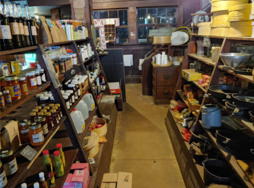 A rustic store interior with wooden shelves filled with jars, bottles, and kitchenware, creating a cozy atmosphere.