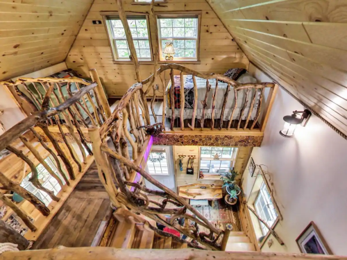 Cozy wooden interior of a cabin with a spiral staircase, large windows, and a lofted sleeping area.