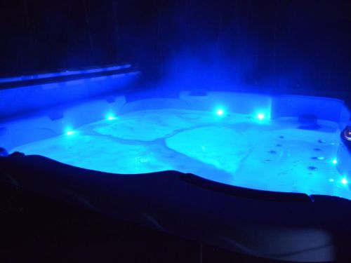 A lit hot tub at night, with blue lights illuminating the bubbling water and steam rising in the dark surroundings.