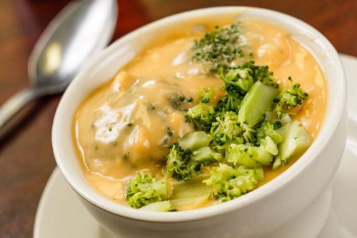 A bowl of creamy soup with broccoli and dumplings, garnished with herbs, served on a white plate.