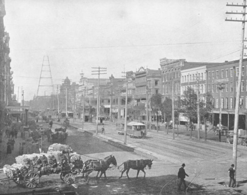 Historic street scene with horse-drawn carts, early electric poles, and a tram in a bustling urban setting.