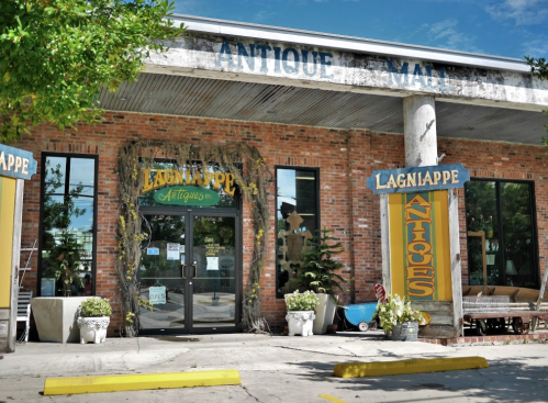 Exterior of Lagniappe Antiques store, featuring brick walls, large windows, and vibrant signage.