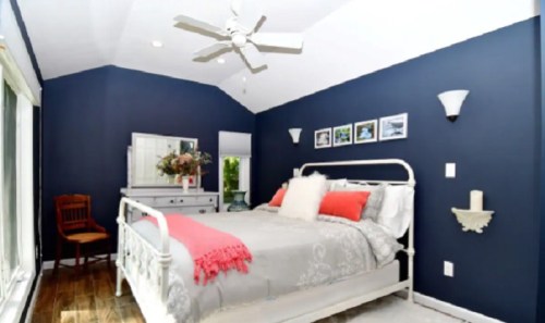 Cozy bedroom with a white bed, navy walls, decorative photos, and a wooden chair by a large window.