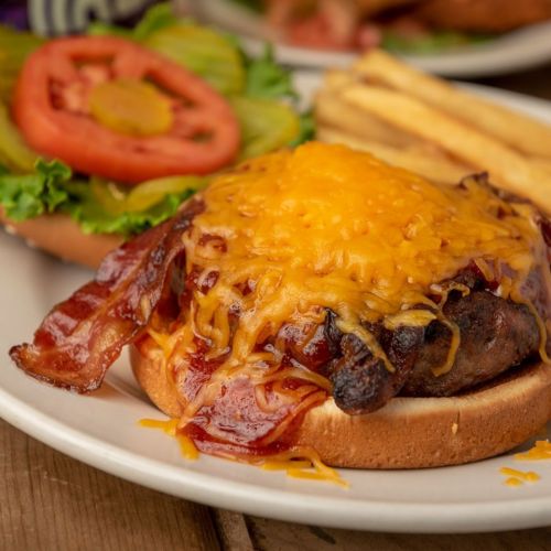 A juicy burger topped with melted cheese and bacon, served with fries and a side of lettuce and tomato.