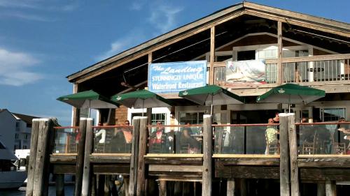 A waterfront restaurant with a wooden deck, green umbrellas, and a sign reading "The Landing: Stunningly Unique."