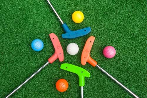 Colorful mini golf putters and balls arranged on green turf.