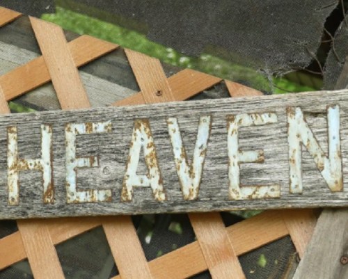 A weathered wooden sign with the word "HEAVEN" painted in white letters.