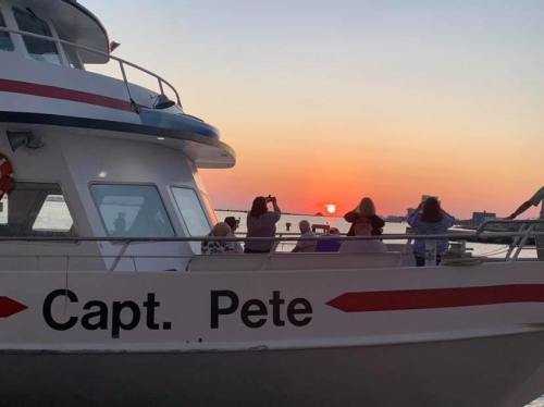 A boat named "Capt. Pete" with people watching a sunset over the water.