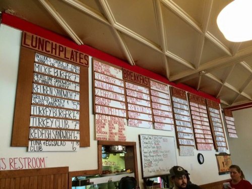 Menu board displaying lunch and breakfast items with prices, featuring sandwiches, burgers, and daily specials.