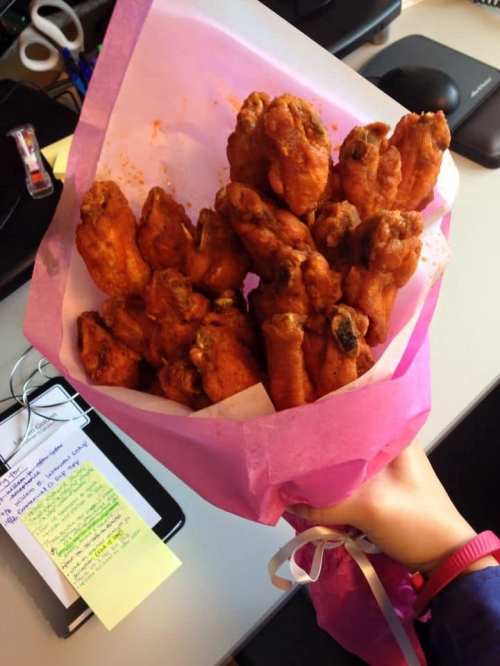 A hand holding a bouquet made of fried chicken wings wrapped in pink paper.