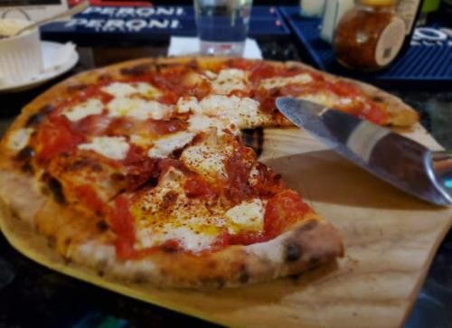 A freshly baked pizza with melted cheese and tomato sauce, sliced on a wooden board, with a knife beside it.