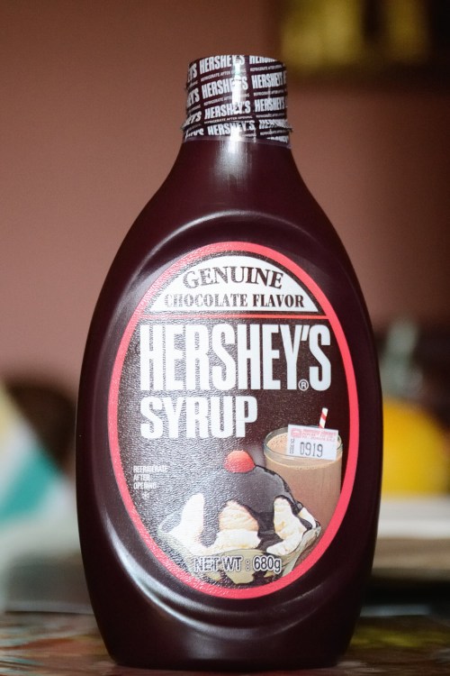 A bottle of Hershey's chocolate syrup with a label featuring the brand name and a dessert illustration.