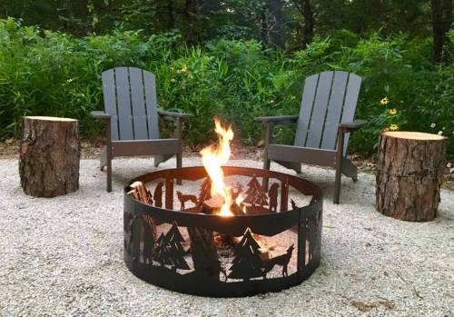 A cozy fire pit surrounded by two chairs and tree stump seats, set in a natural, green outdoor space.