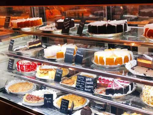 A display case filled with various cakes and pies, each labeled with small signs, showcasing a variety of desserts.