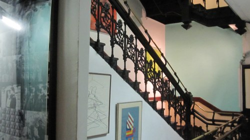 A staircase with ornate iron railings, surrounded by colorful artwork and walls in a gallery setting.
