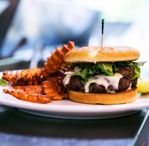 A juicy burger with lettuce and cheese, served with crispy waffle fries on a white plate.