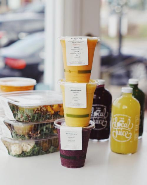 Three stacked smoothie cups in vibrant colors, with salad containers and juice bottles in the background.