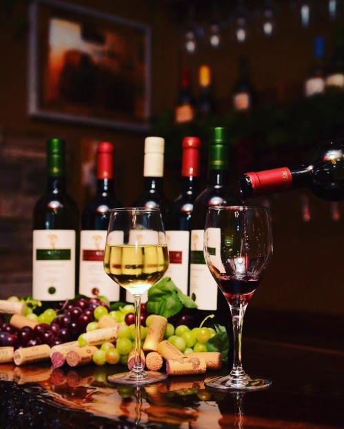 A selection of wine bottles with two glasses filled with white and red wine, surrounded by grapes and corks.