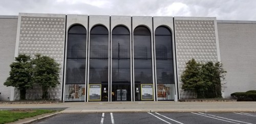 Front view of a large, modern building with arched windows and a textured facade, surrounded by greenery.