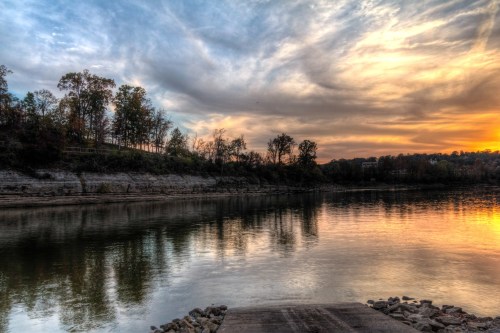 A serene river scene at sunset, with colorful clouds reflecting on the water and trees lining the shore.