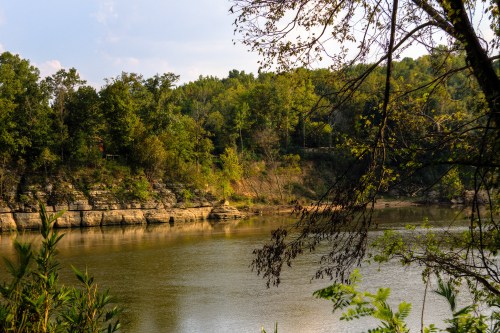 A serene river scene surrounded by lush greenery and rocky cliffs under a clear sky.