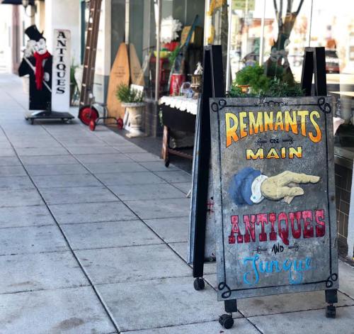 A sidewalk sign for "Remnants on Main" advertising antiques and junk, with decorative elements and a vintage aesthetic.