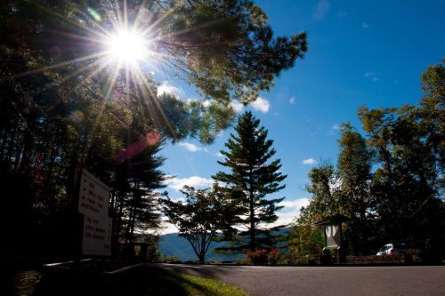 Sunlight filters through trees, illuminating a scenic view of mountains and a clear blue sky.