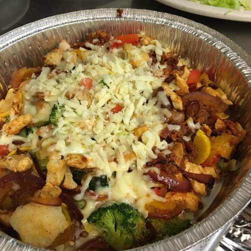 A colorful dish with chicken, vegetables, and melted cheese in a foil container.
