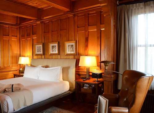 Cozy hotel room with wooden walls, a king bed, bedside lamps, and a comfortable armchair.