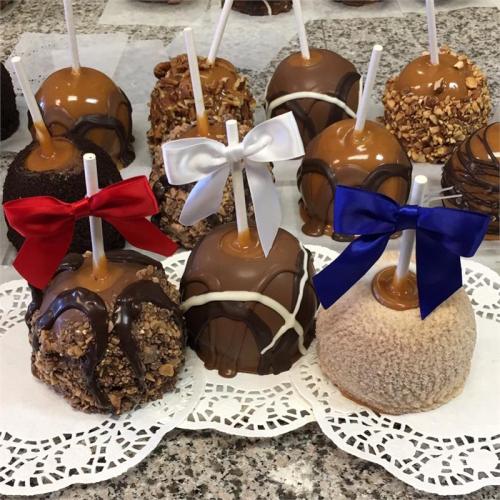 A variety of caramel apples decorated with chocolate, nuts, and colorful bows on a lace doily.