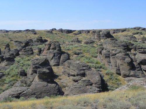 Rocky formations rise from a grassy landscape under a clear blue sky, showcasing unique geological features.