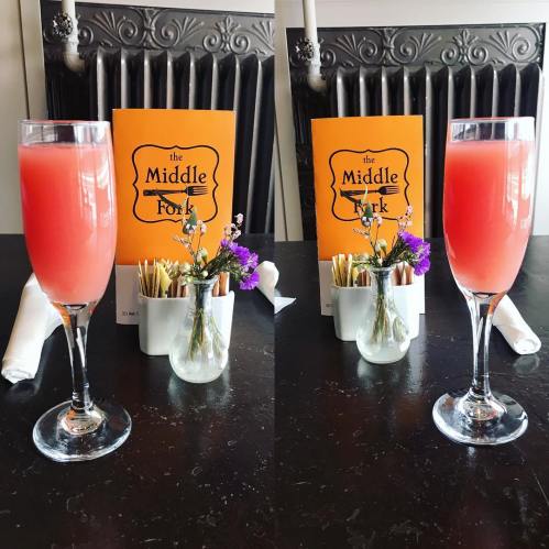 Two glasses of pink drinks on a table with a menu and a small vase of flowers.
