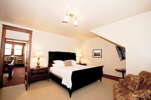 Cozy bedroom featuring a large bed, nightstands, a sofa, and warm lighting in a softly colored room.