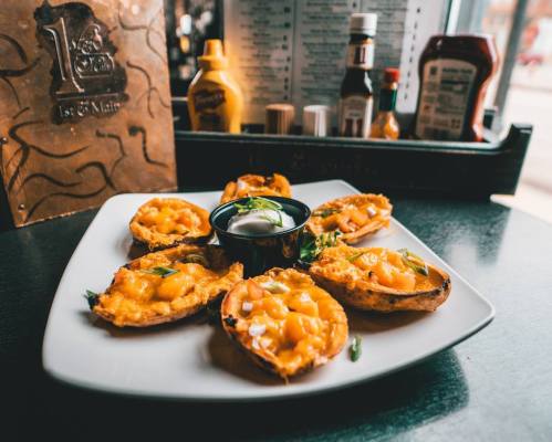 A plate of cheesy nachos topped with diced ingredients and served with a dipping sauce, set against a restaurant backdrop.