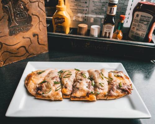 A plate of flatbread topped with melted cheese, sliced meat, and green onions, served in a restaurant setting.