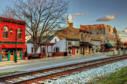 A quaint street lined with colorful buildings and shops, alongside a railway track under a clear sky.