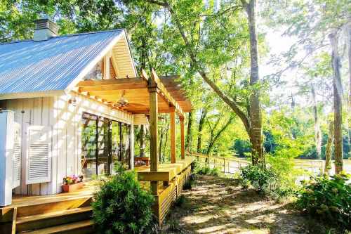 A cozy cabin with a wooden deck surrounded by lush greenery and trees, illuminated by sunlight.