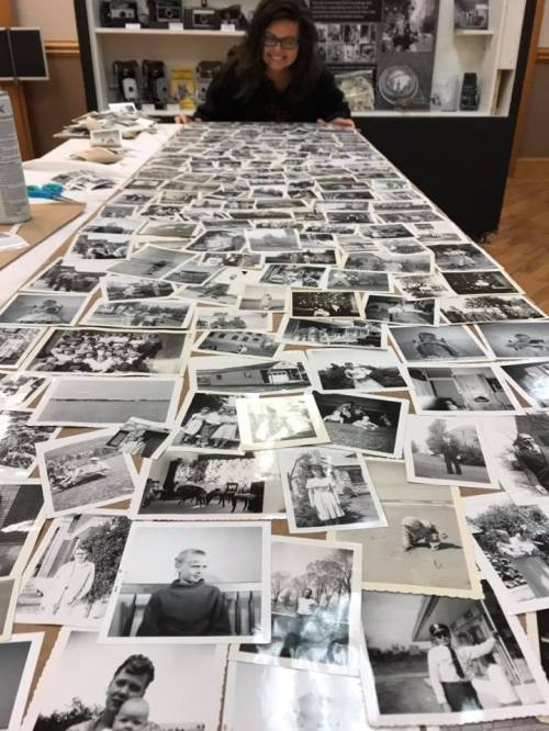 A person examines a long table covered with numerous black-and-white photographs.