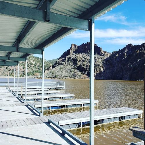 A serene lakeside view with docks and rocky mountains in the background under a clear blue sky.