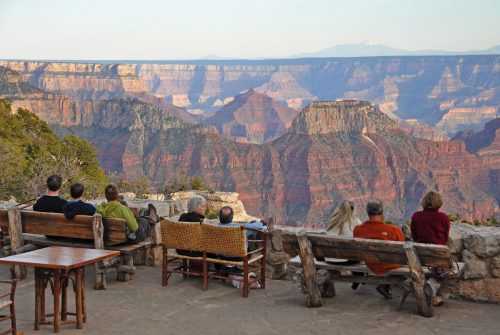 A group of people sitting on benches, enjoying a scenic view of the Grand Canyon at sunset.