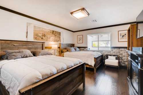 Cozy bedroom with two beds, wooden furniture, and a window, featuring a decorative wall and warm lighting.