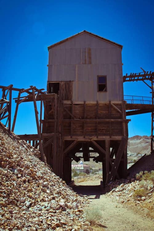 Abandoned wooden structure on stilts, surrounded by rocky terrain under a clear blue sky.