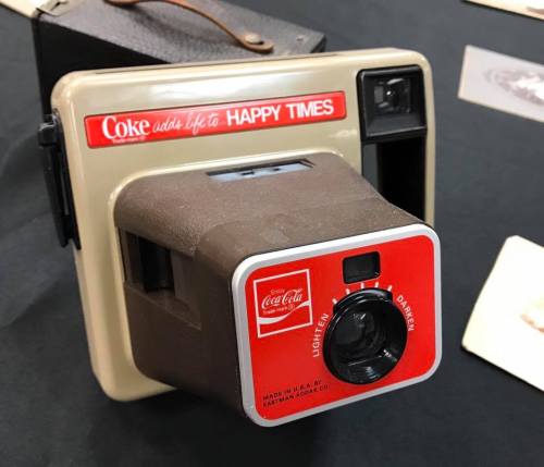 A vintage Coca-Cola camera with a red and beige design, featuring the slogan "Coke adds life to happy times."