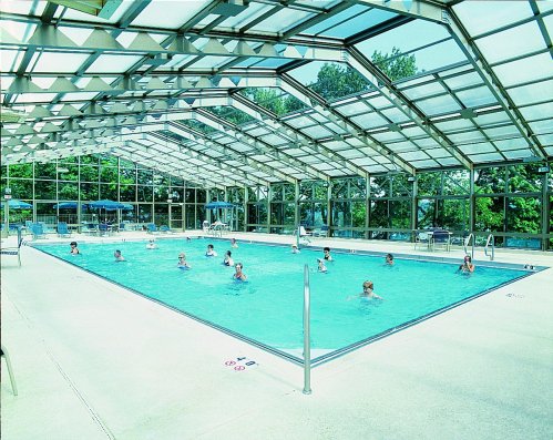 Indoor swimming pool with a glass roof, featuring people swimming and relaxing around the water.